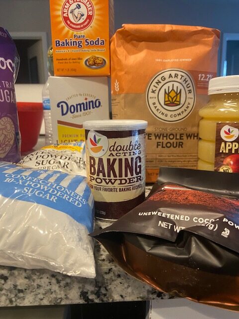 Some of the baking supplies used to make the cake - baking soda, white whole wheat flour, baking powder, light brown sugar, apple sauce, cane sugar, confectioner's sugar, and cocoa powder